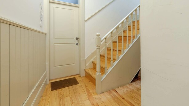 A hallway with a white door, a wooden floor, and a white staircase with a wooden handrail. - Historic Se Apartment Prime Location by HostWise (Sé)
