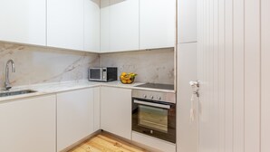 A compact kitchen with white cabinetry, a built-in microwave, a stove, and a sink. - Historic Se Apartment Prime Location by HostWise (Sé)