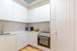 Uma cozinha compacta com armários brancos, micro-ondas embutido, fogão e pia.