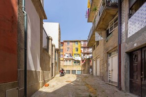 Uma rua estreita com edifícios de ambos os lados, uma moto estacionada na lateral e roupas penduradas em varandas.