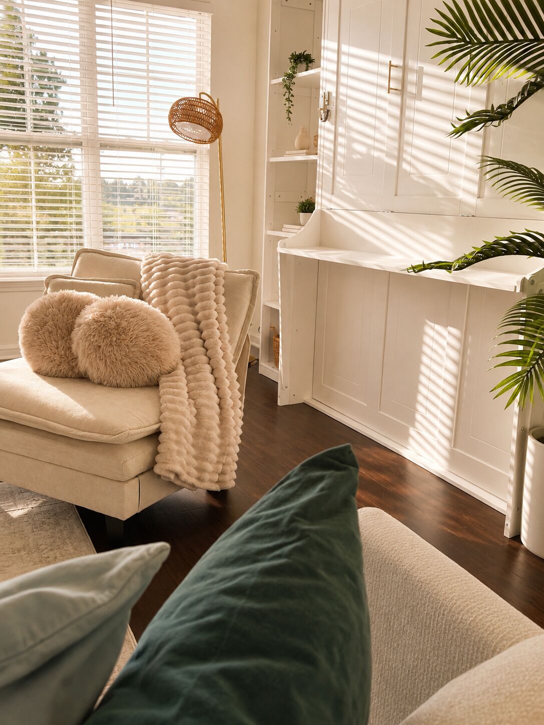 A modern living room with a sofa, a large fluffy throw blanket, a floor lamp, and a view of a white cabinet with shelves.