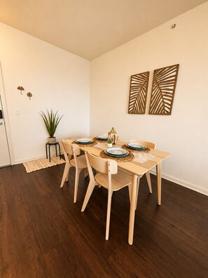A dining area with a wooden table set for four, surrounded by chairs.