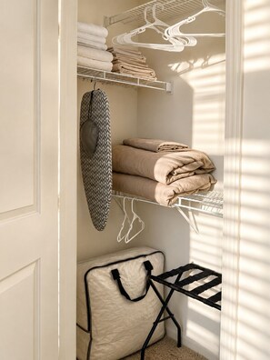 A neatly organized storage closet with shelves for folded towels and a hanging garment rack.