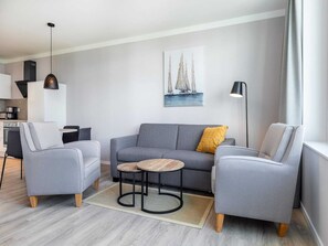 A modern living room with a grey sofa, two armchairs, a small coffee table, and a painting of sailboats on the wall. - Ubernachtung mit Sauna und Westloggia (Lübeck)