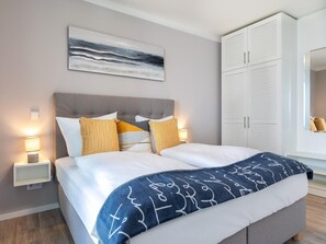 A modern bedroom with a bed, bedside lamps, a headboard, a wardrobe, and a painting on the wall. - Ubernachtung mit Sauna und Westloggia (Lübeck)