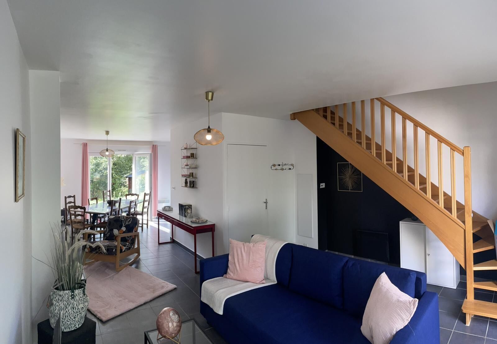 Un salon avec un canapé bleu, une table à manger avec des chaises, un escalier et une porte avec un porte-manteau.