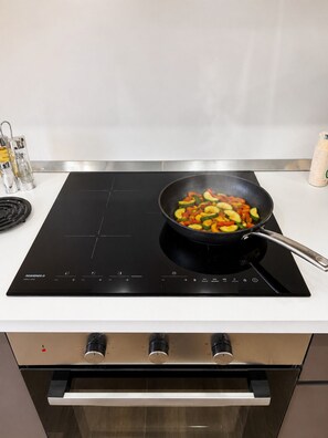 A kitchen with an induction cooktop, a frying pan with vegetables, and a salt shaker. - Riace Mare – Premium | 100 m from the beach (Riace Marina)