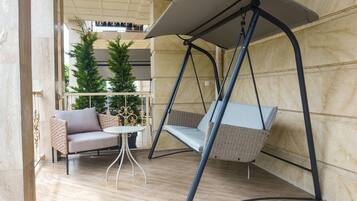 A swing chair with a canopy, a wicker sofa, and a small round table in a room with tiled flooring and a wooden wall.