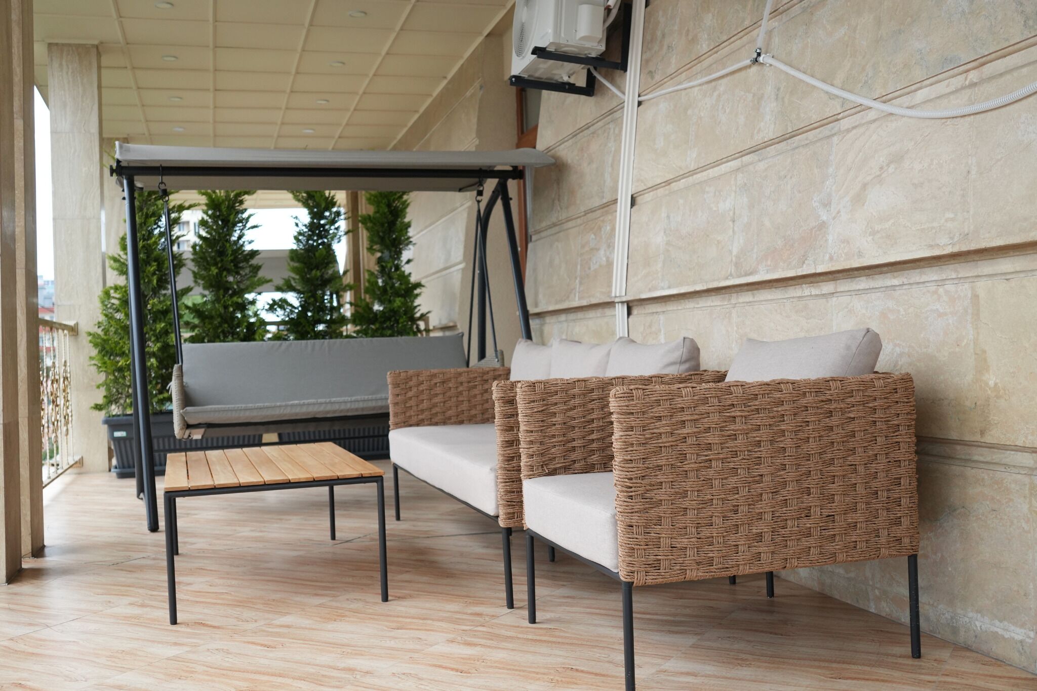 Et moderne udendørs opholdsområde med sofa og bord, en pergola samt udsigt til grøn bevoksning.