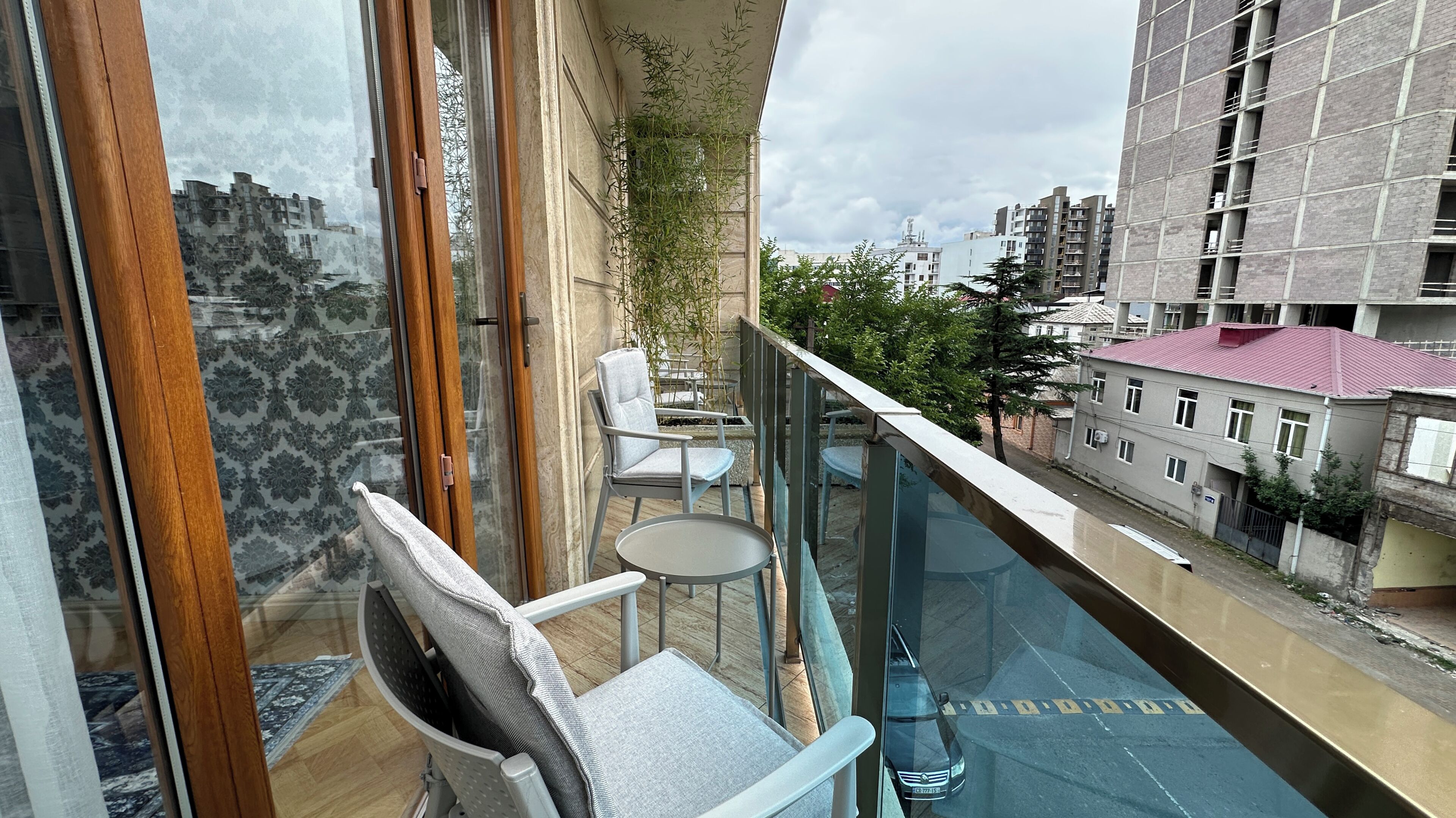 A balcony with a view of the city, a chair, a small table, and a railing.