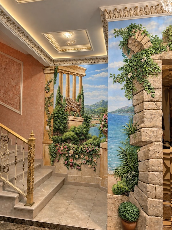 Una imponente escalera con barandillas ornamentadas y un mural que representa una escena clásica con columnas y un paisaje.