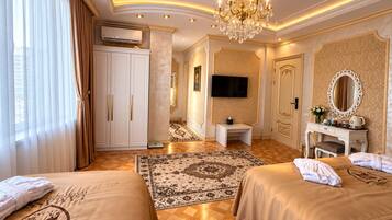A hotel room with two beds, a television, a desk, a mirror, and a chandelier.