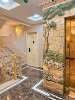 Una entrada imponente con una escalera de mármol, una pared decorativa con un árbol y flores artificiales, y una puerta con el número 206.