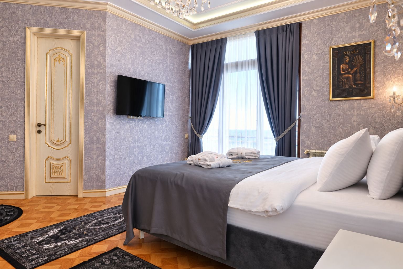 Une chambre d’hôtel comprenant un lit, un téléviseur à écran plat, une porte ornée de panneaux décoratifs et un tapis à motifs.