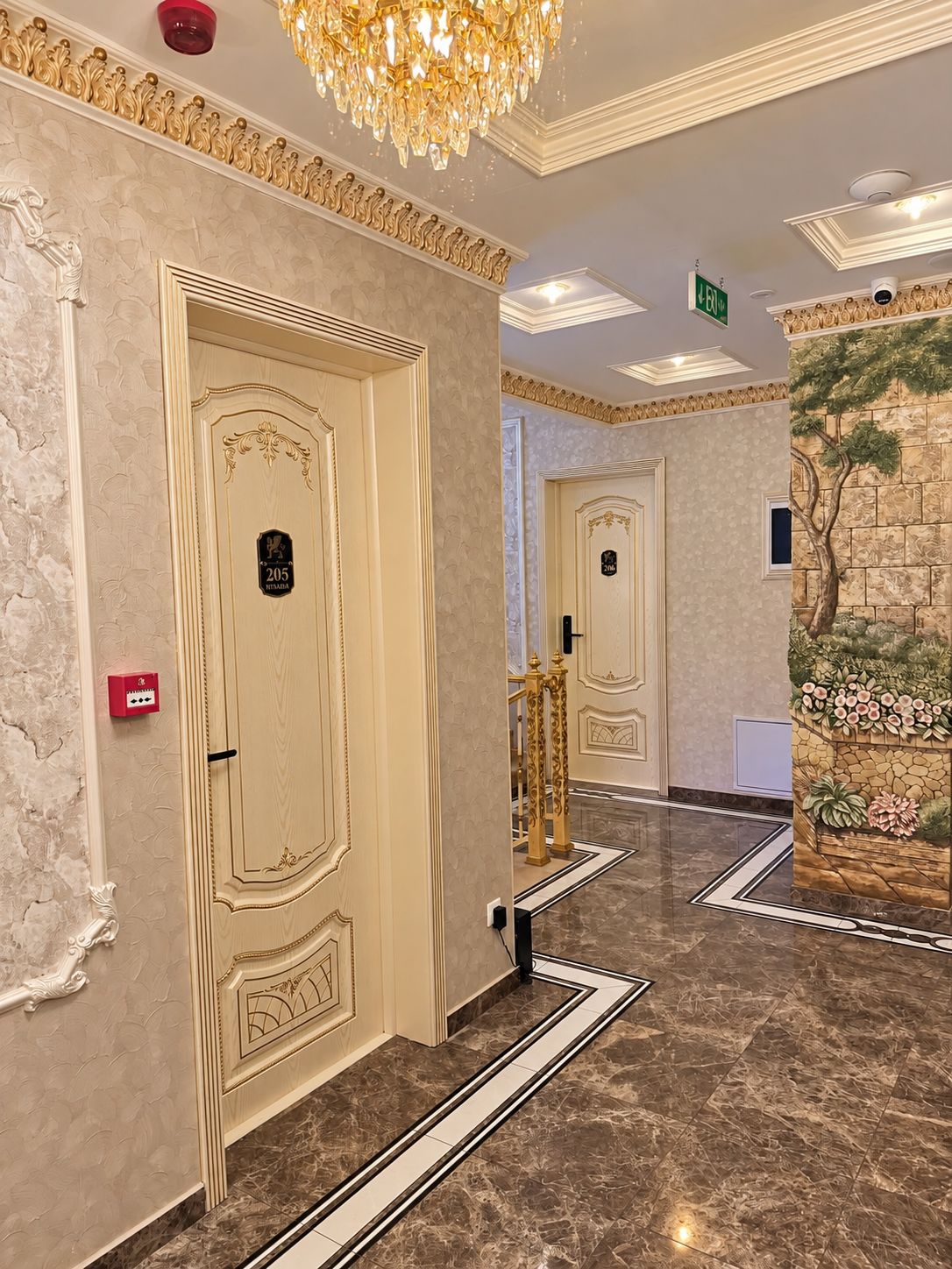 A hotel corridor with ornate doors, a chandelier, and a decorative wall.