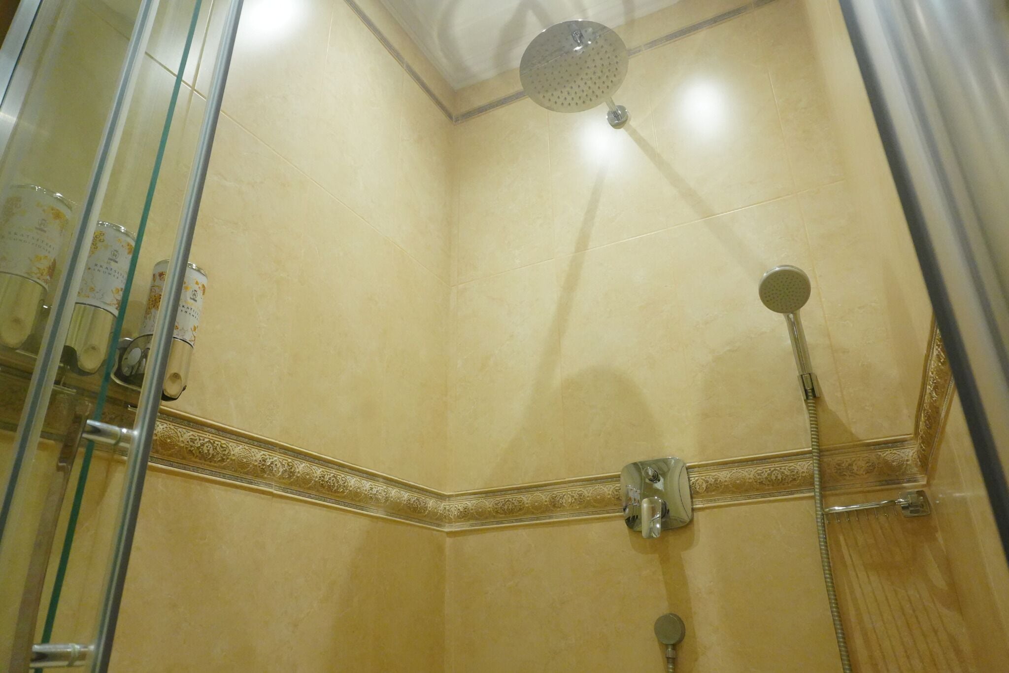 Un rincón de un baño con mampara de vidrio, ducha de mano y grifo empotrado.