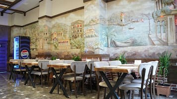 Un restaurante con un mural de una escena costera, mesas con sillas y un refrigerador de Pepsi.