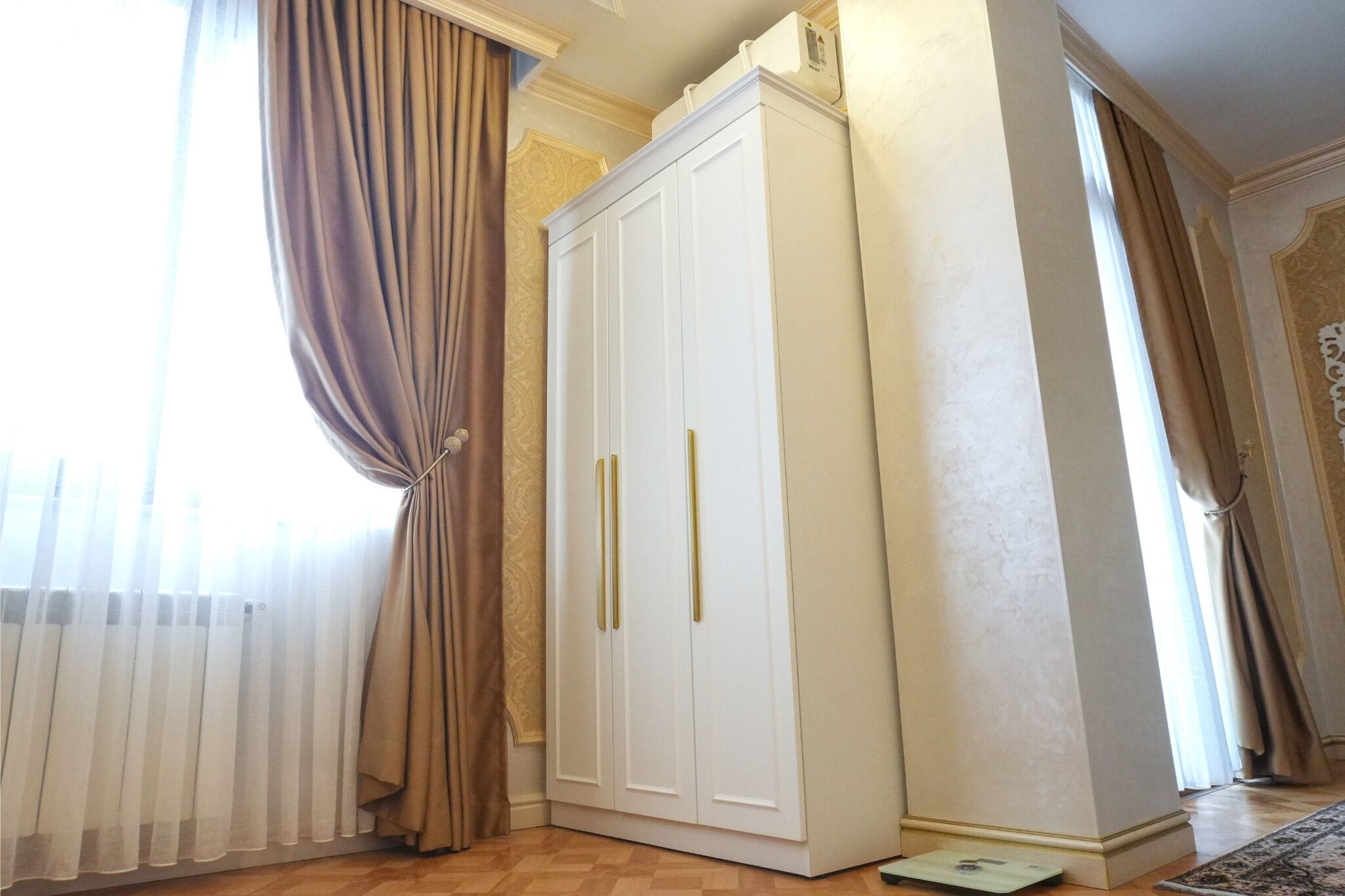 A room with a white wardrobe, a radiator, and a window with curtains.
