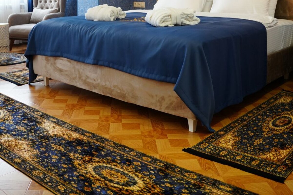 A bedroom with a large bed, a chandelier, a blue patterned wall, and a painting.