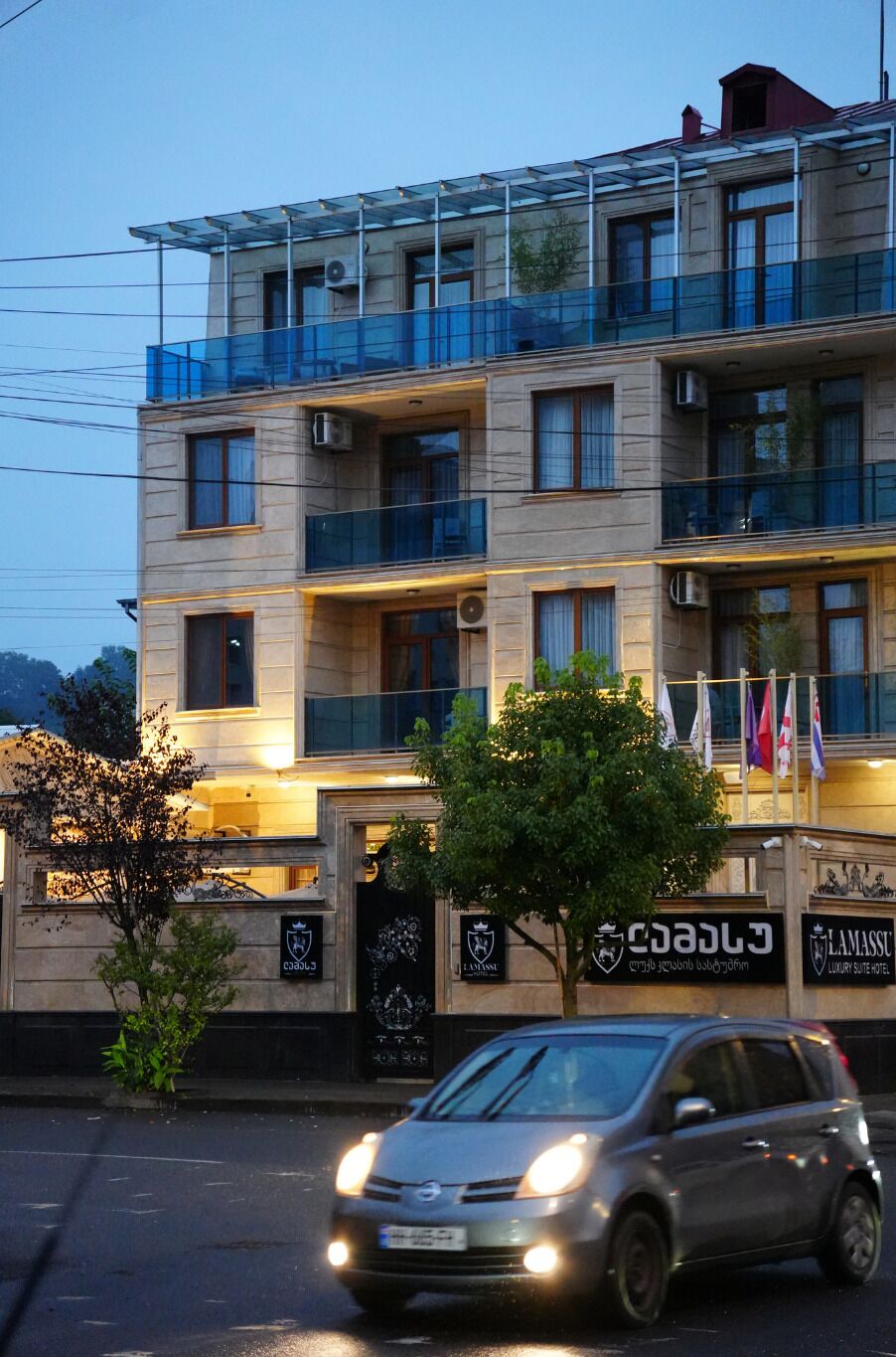 A multi-story hotel with balconies, a car in front, and flags.