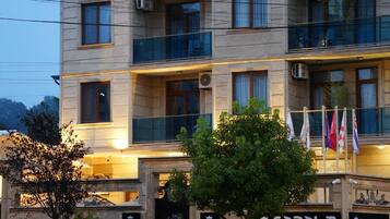 A multi-story hotel with balconies, a car in front, and flags.