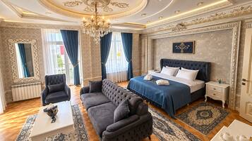 Una lujosa habitación de hotel con una cama grande, una zona de estar con sofá, una mesa de comedor y un candelabro.