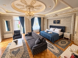 Una lujosa habitación de hotel con una cama grande, una zona de estar con sofá, una mesa de comedor y un candelabro.