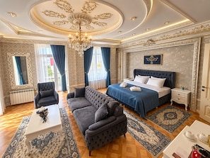 Una lujosa habitación de hotel con una cama grande, una zona de estar con sofá, una mesa de comedor y un candelabro.