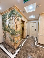 Un vestíbulo con suelo de mármol, una pared decorativa con follaje artificial y una señal de salida.