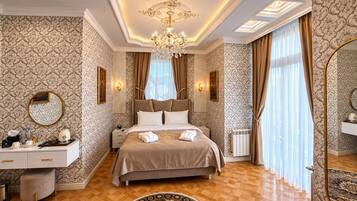 A luxurious bedroom with a large bed, a chandelier, a vanity with a mirror, and a patterned carpet.
