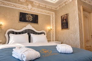 A luxury hotel room with a large bed, ornate headboard, and decorative wall panels.