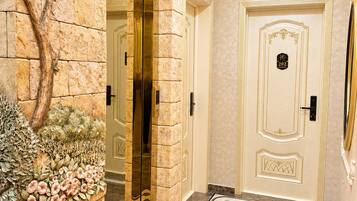 Un vestíbulo de hotel con piso de mármol, una pared decorativa con plantas, un ascensor de vidrio y una puerta con placa de identificación.
