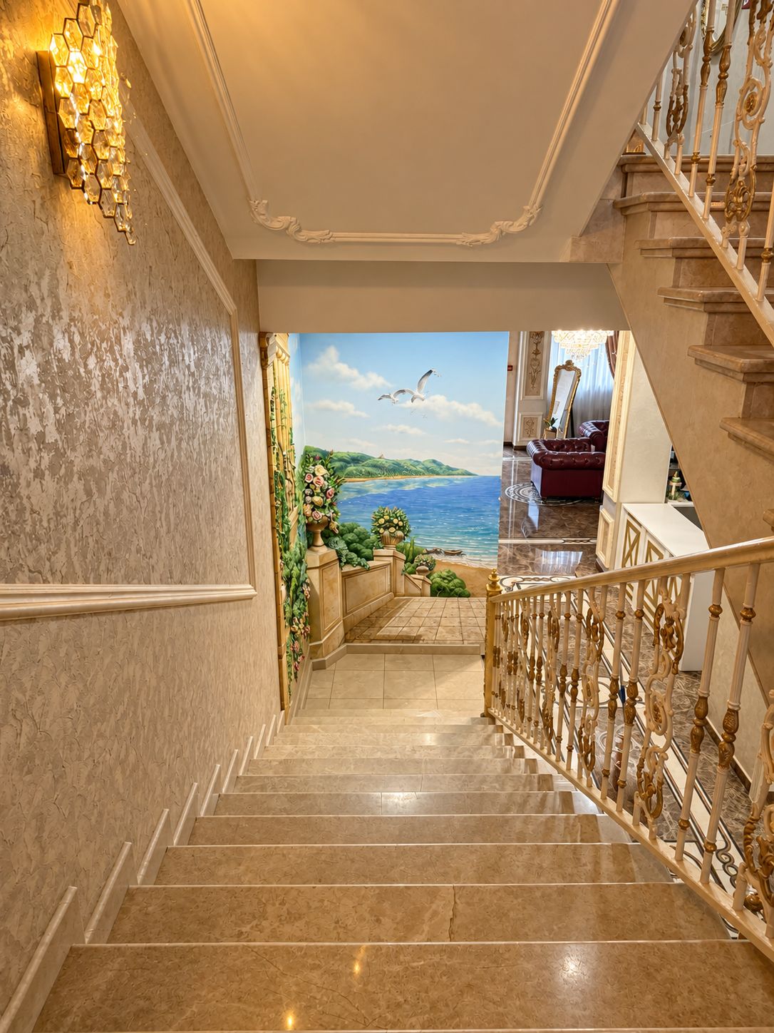 Uma escadaria imponente com vista para uma pintura de paisagem marinha, que leva a um quarto com um sofá vermelho e um candelabro.