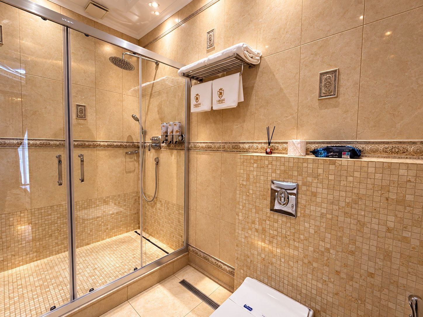 Un baño de hotel con ducha de vidrio, un perchero con una toalla y un dispensador de jabón en la pared.