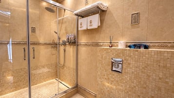 Un baño de hotel con ducha de vidrio, un perchero con una toalla y un dispensador de jabón en la pared.