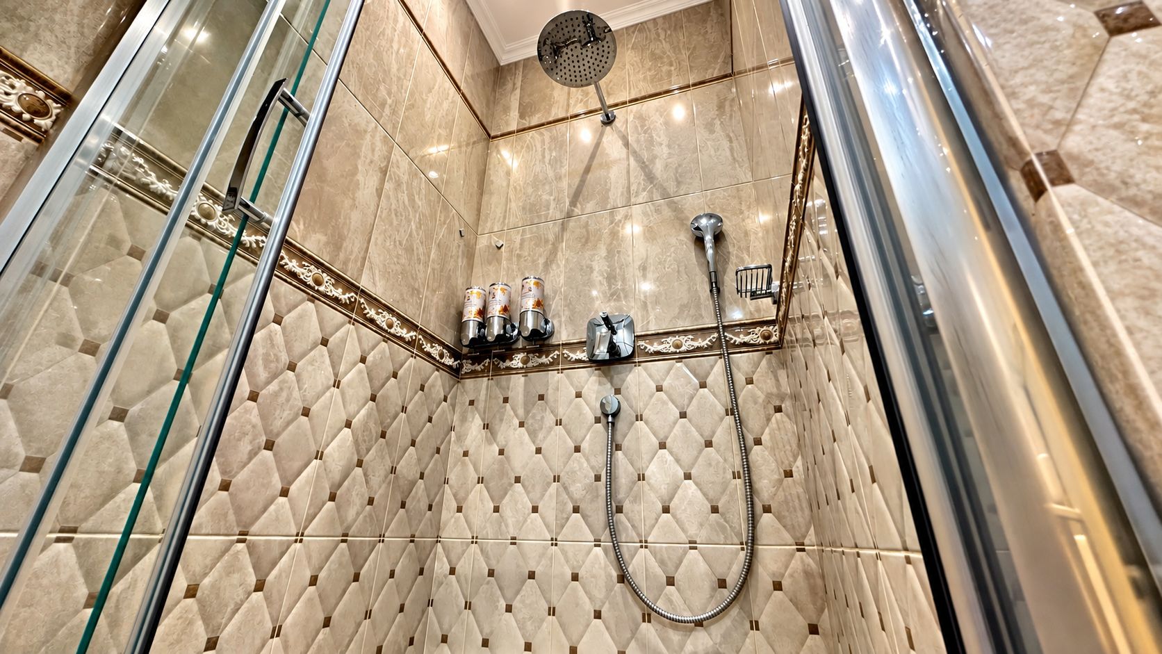A shower area with a glass door, a showerhead, a handheld shower, and a wall-mounted control panel.