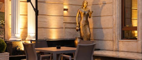 An outdoor seating area with a statue, tables, and chairs.
