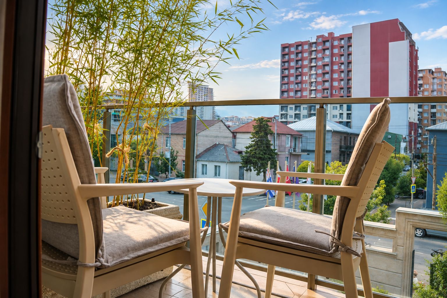 A balcony with two chairs and a small table, overlooking a cityscape with buildings and a clear sky.
