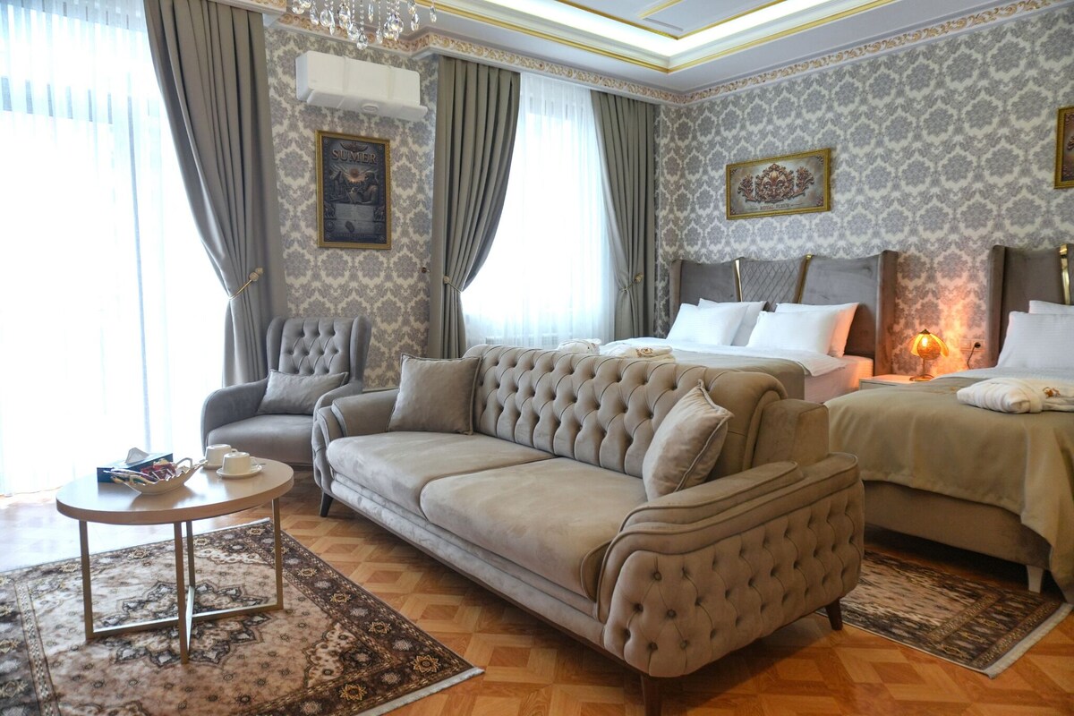 A hotel room with a large bed, a sofa, a small table, and a chandelier.