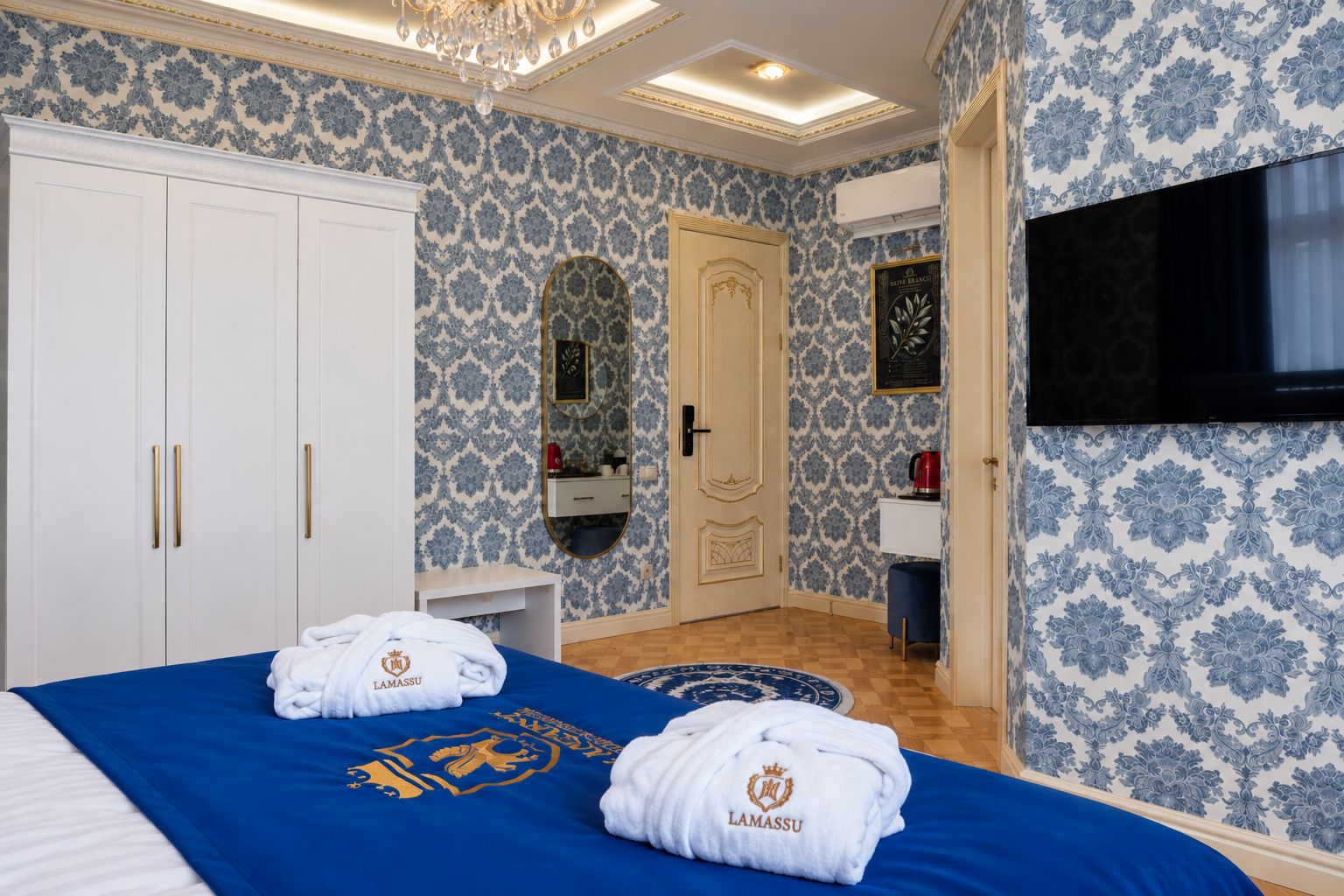 A hotel room with a bed, a wardrobe, a mirror, a television, and a patterned wall.