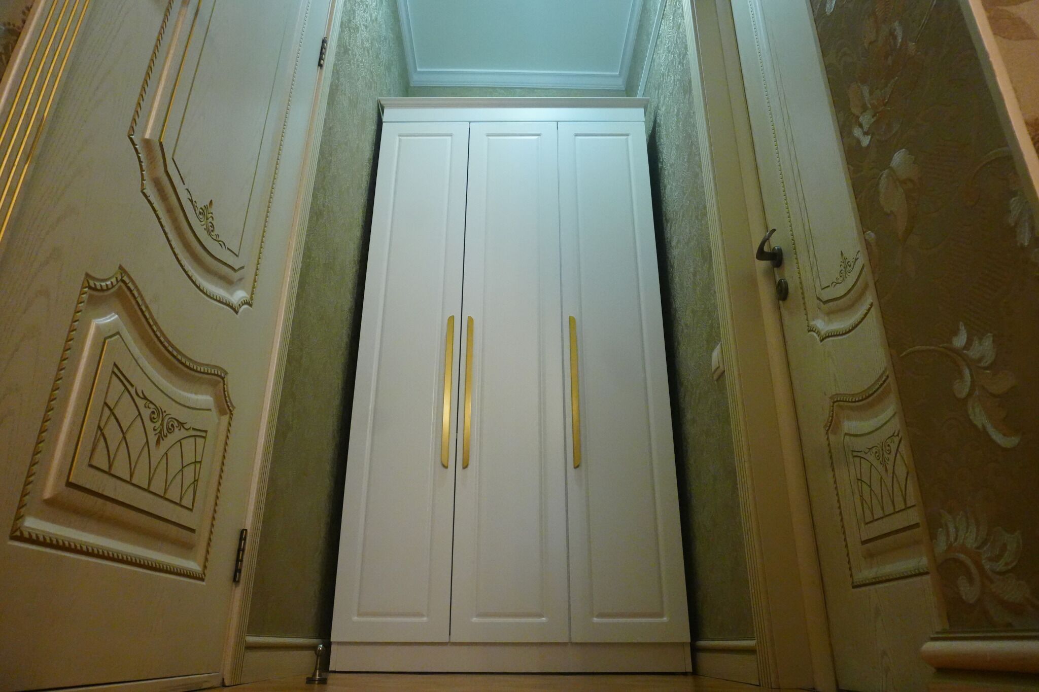 Un armario blanco con dos pomos, flanqueado por molduras decorativas y una pared con diseño.