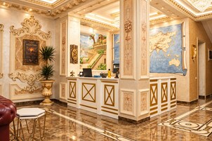 A luxurious lobby with ornate gold detailing, a reception desk, a large world map, and a mural of a classical building.