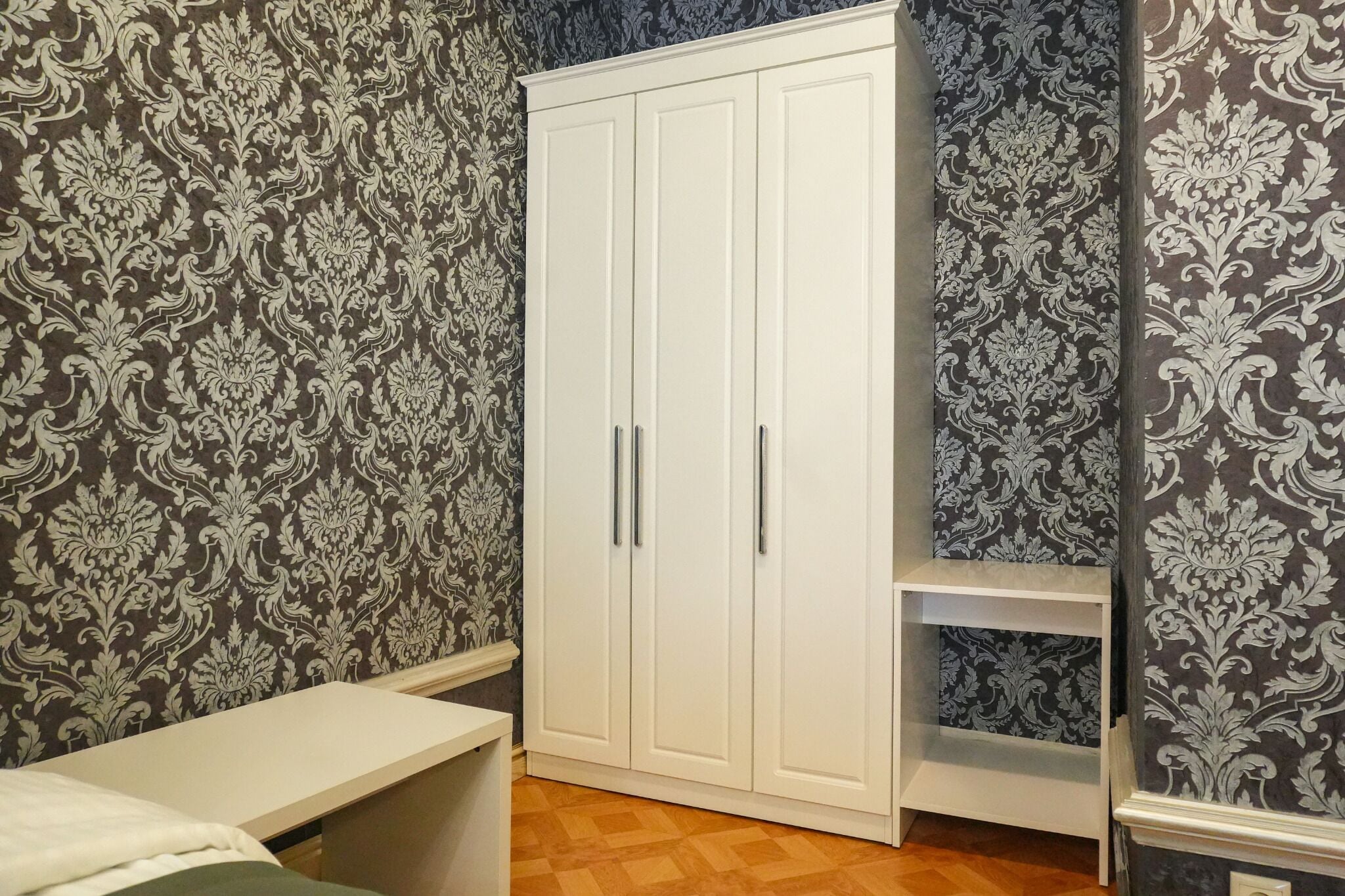 A room with a wardrobe, a small table, and patterned wallpaper.