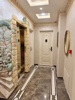 Un pasillo con piso de mármol, pared de piedra con un mural de un árbol y una puerta con una placa numérica.