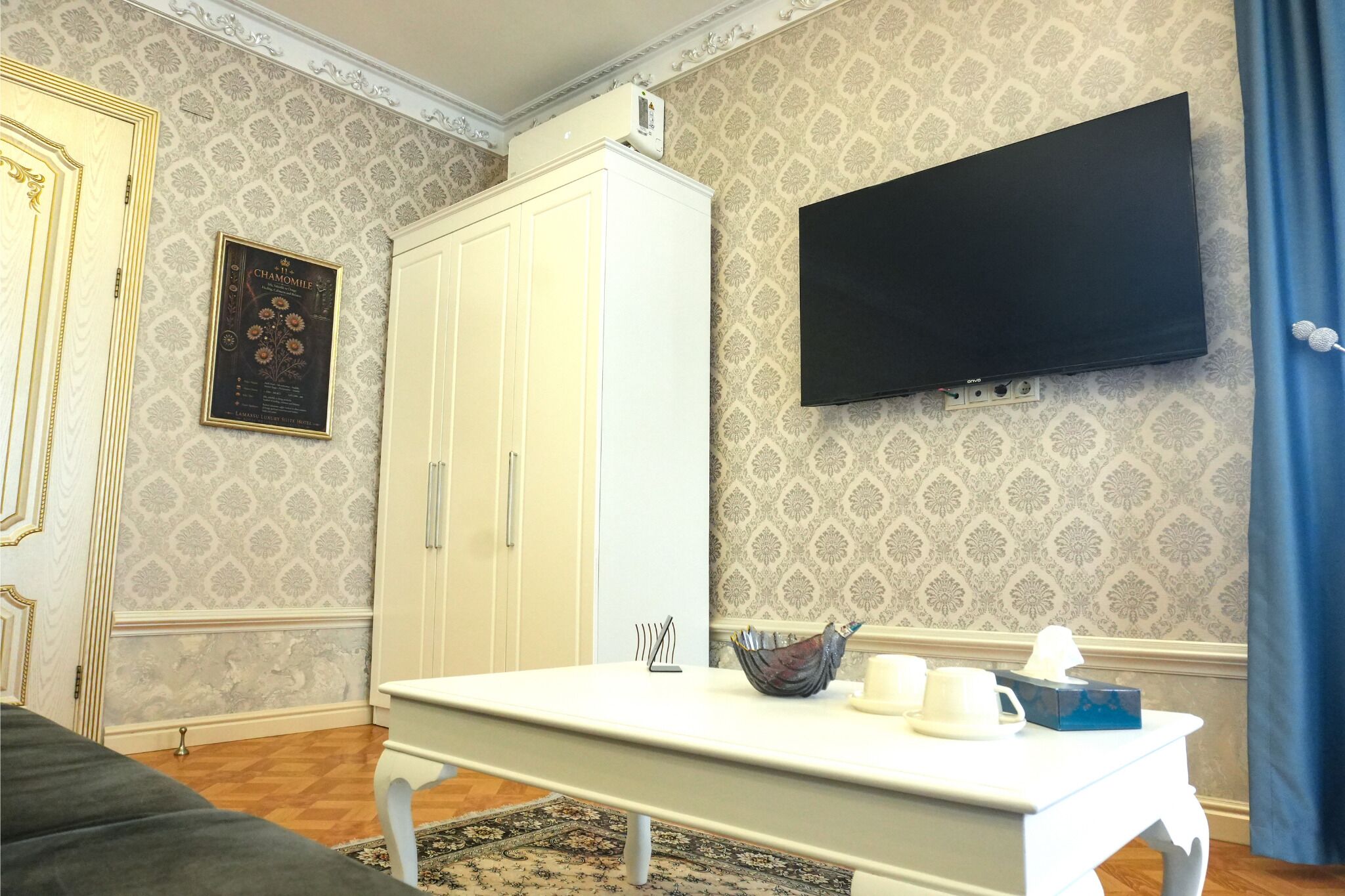 Una habitación con una mesa blanca, un televisor montado en la pared y un papel tapiz estampado.