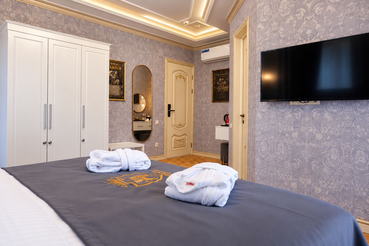 Une chambre d’hôtel comprenant un lit, deux serviettes, une télévision, une armoire, un miroir et une porte ornée d’un cadre décoratif.
