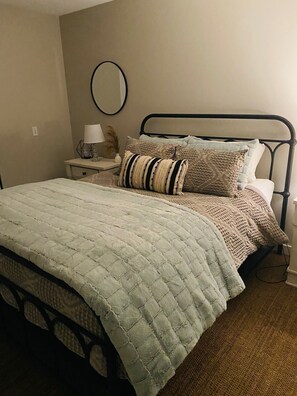 Ein Schlafzimmer mit einem Bett, einem Nachttisch, einer Lampe und einem an der Wand befestigten Spiegel.