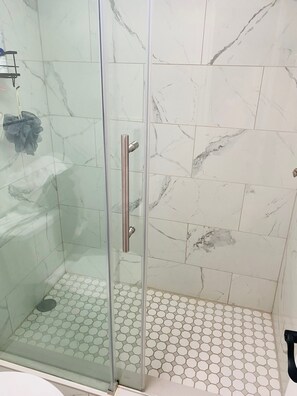 Lasiseinöillä varustettu suihku, jossa on metallinen kahva ja kuusikulmaisista laatoista tehty lattia.