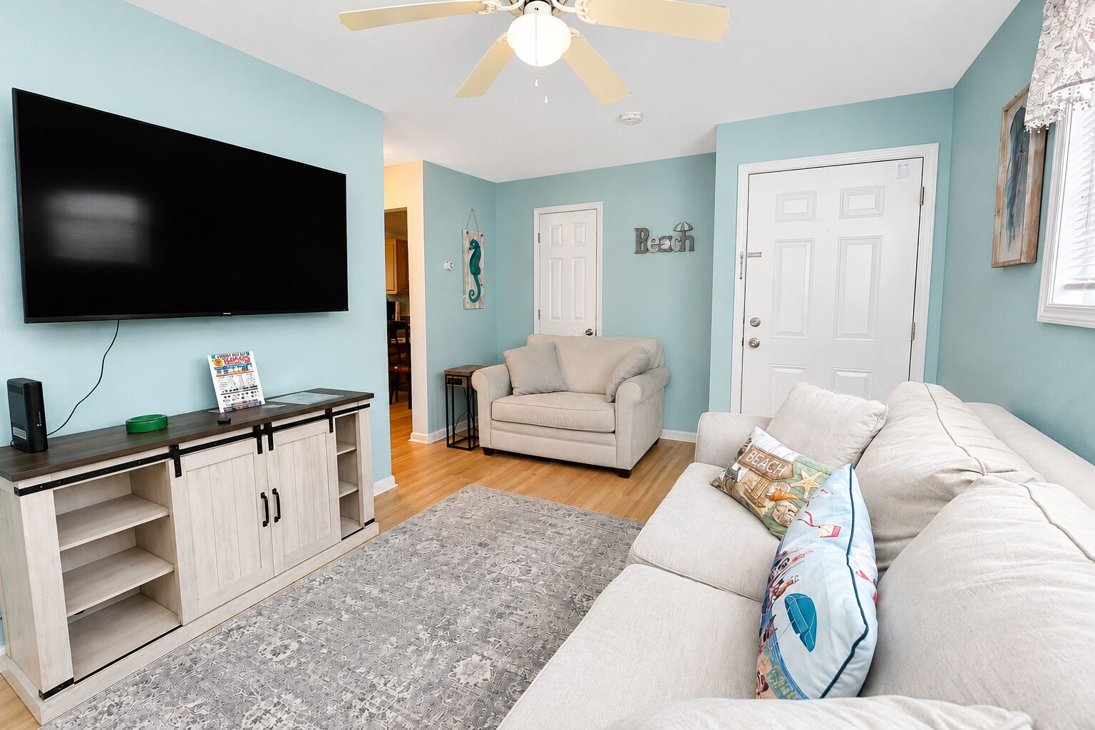 A living room with a flat-screen TV, a sofa, a coffee table, and a ceiling fan.