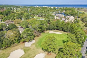 Ein Luftbild eines Golfplatzes mit Sandbunkern, Bäumen und Wohnhäusern im Hintergrund.